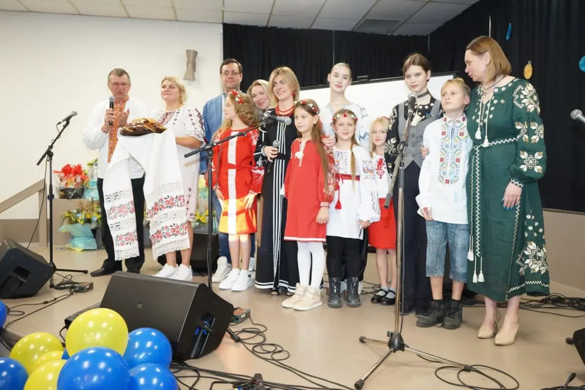 A man holding a decorated ceremonial korovai bread on the UAFest stage, surrounded by children and adults in vyshyvanka gathered around the microphones