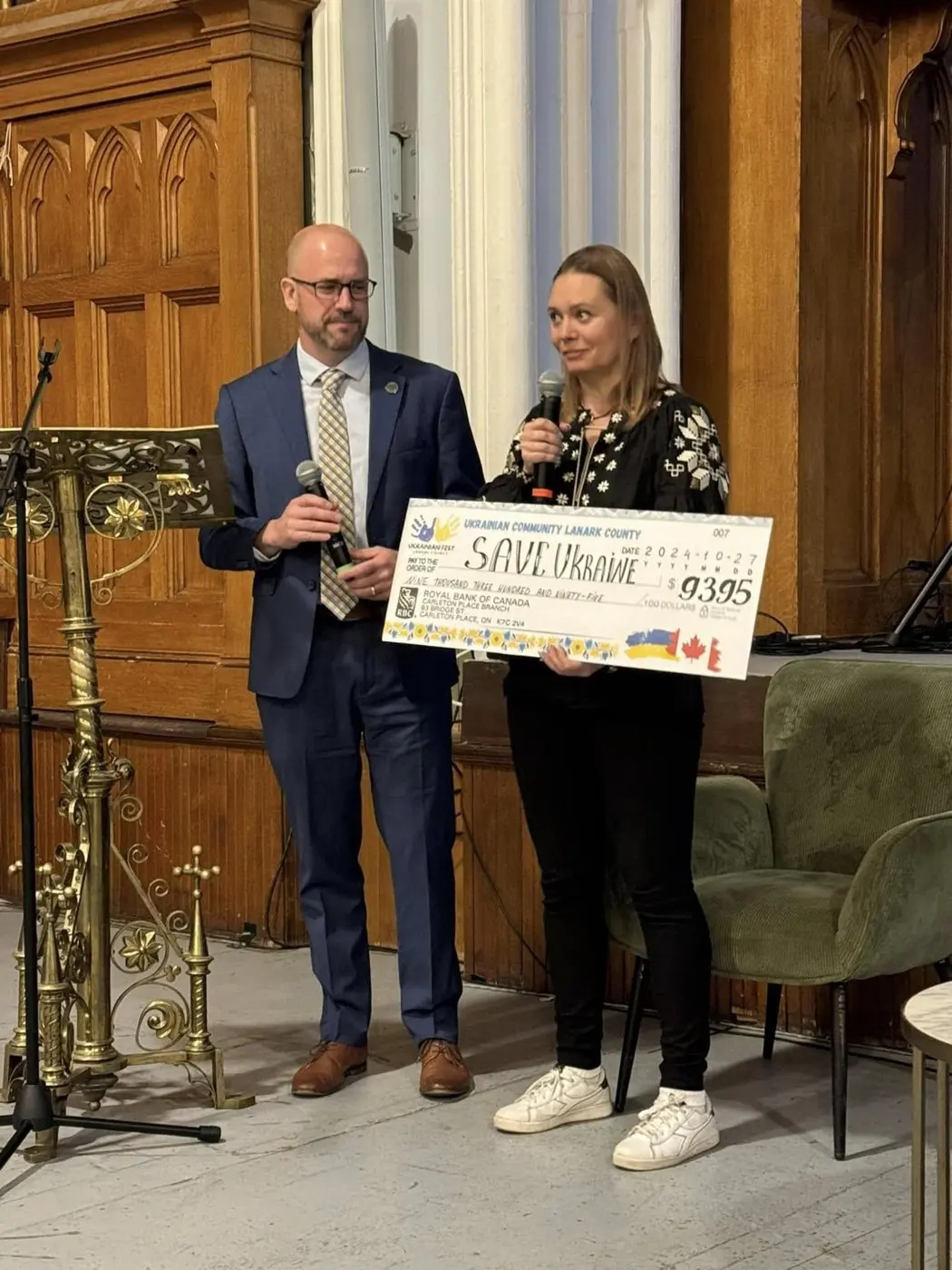 A man in a suit and a woman in an embroidered blouse presenting a large ceremonial cheque for $9,395 to Save Ukraine
