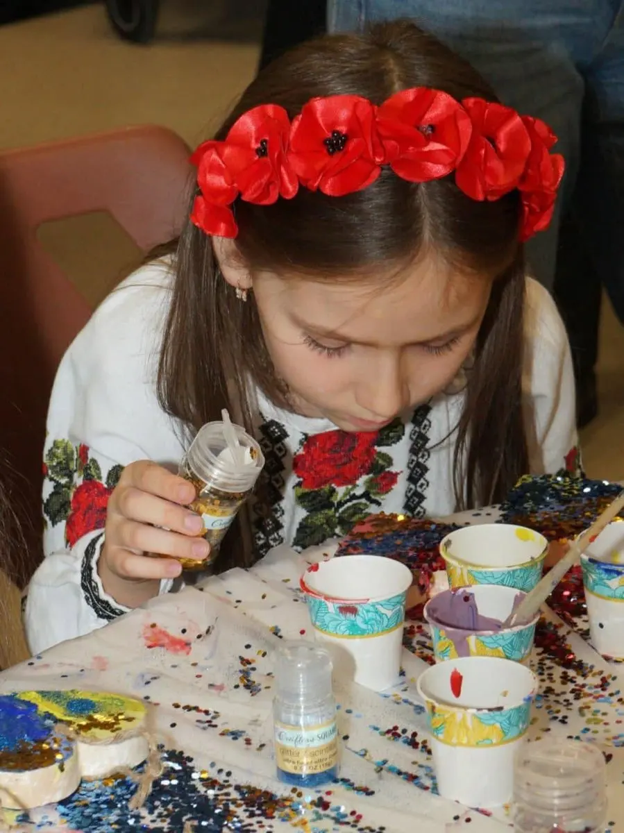 Girl wearing a red poppy flower crown doing a glitter and sequin craft activity at a table at UAFest