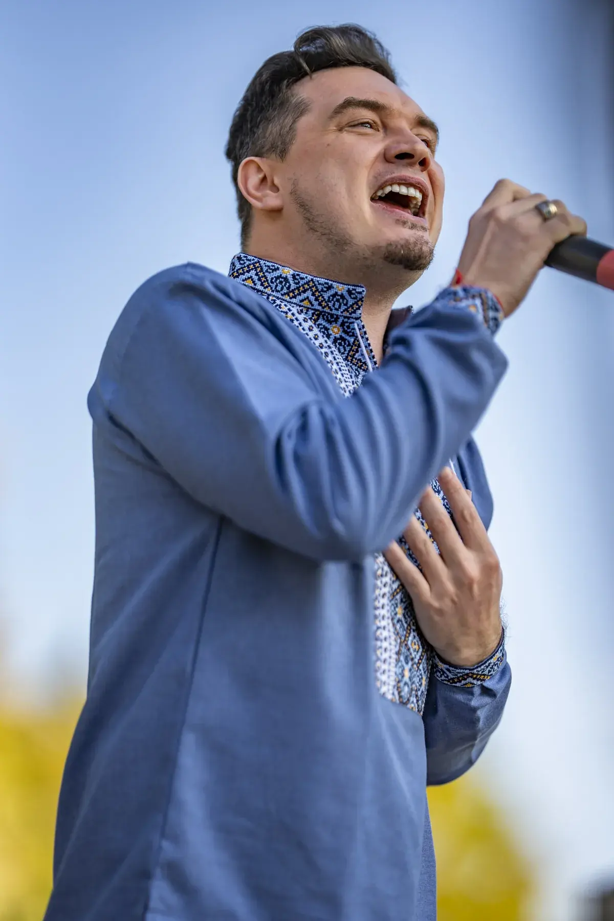 DEN BAURIN at UAFest 2026 — Male singer in a blue vyshyvanka sings against the sky, hand on chest (photo: Tim Skinner)