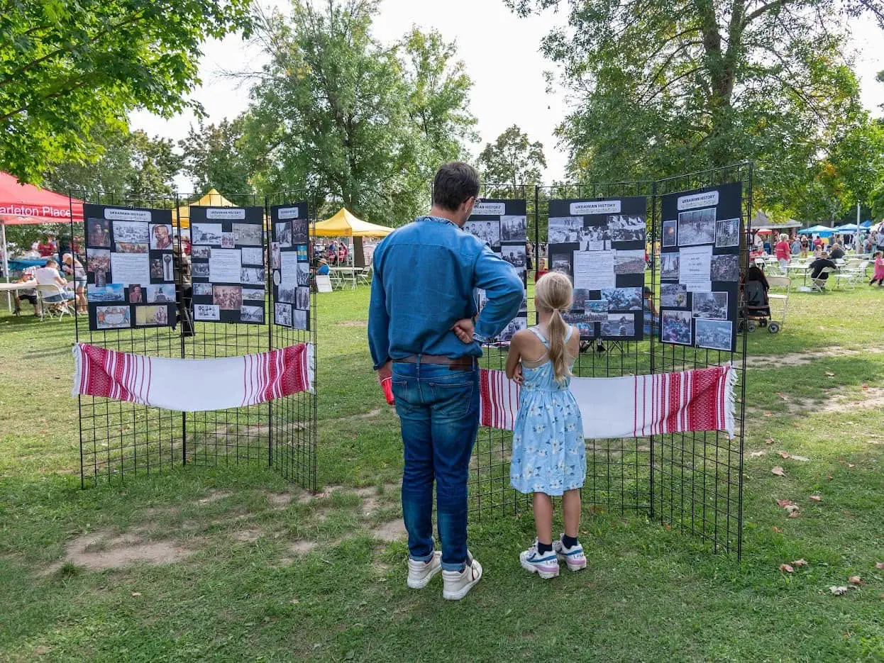 A father and daughter reading illustrated Ukrainian history display boards set up on the festival grounds