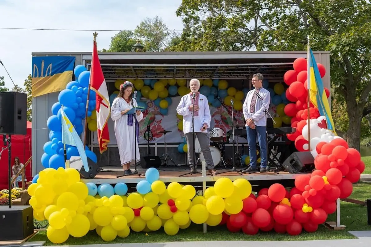 Hosts speaking on the UAFest Main Stage, decorated with Ukraine and Canada flags and a rainbow of balloon garlands, with a band set up behind them
