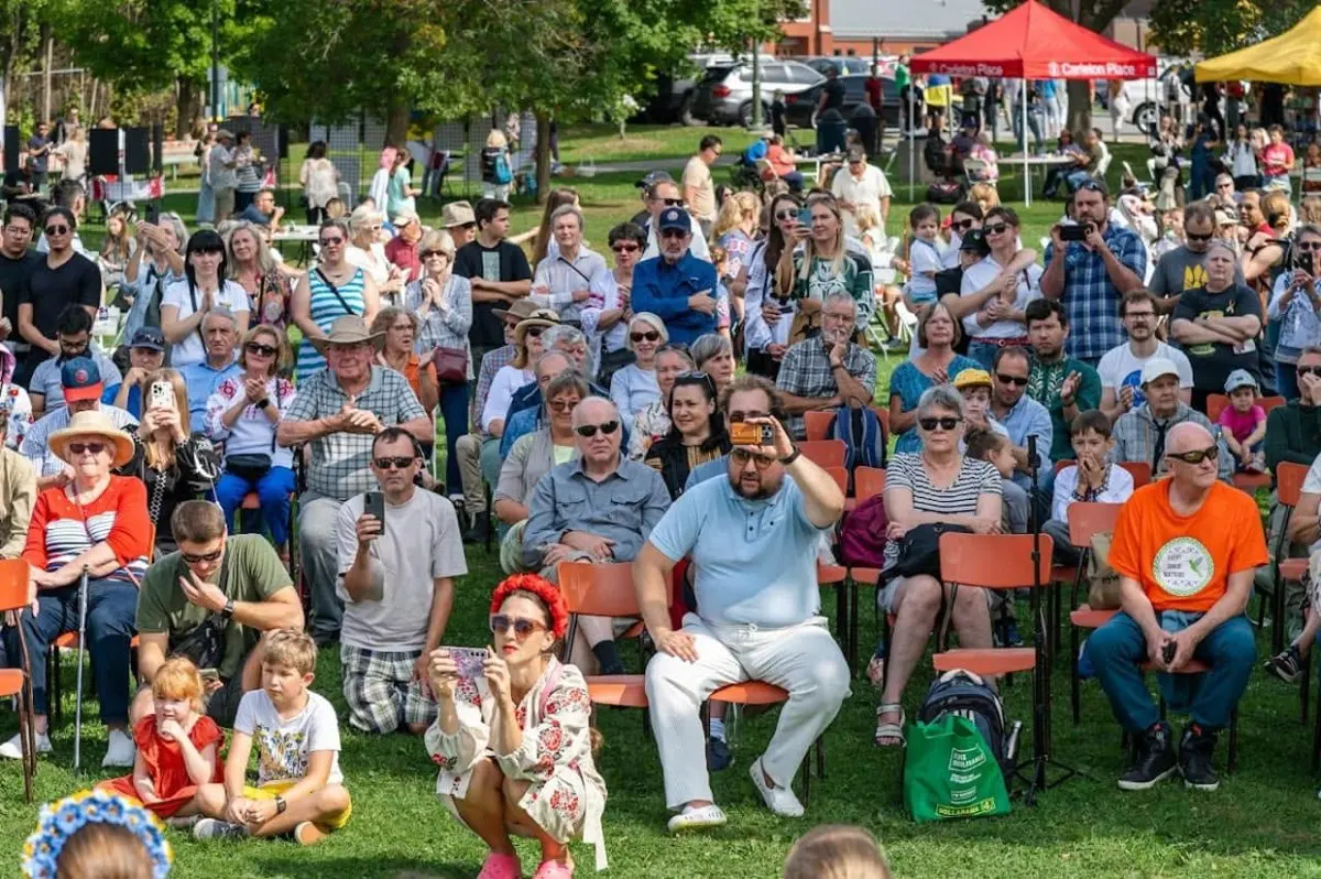 A large seated crowd of festival-goers, including children, watching a performance on the festival grounds