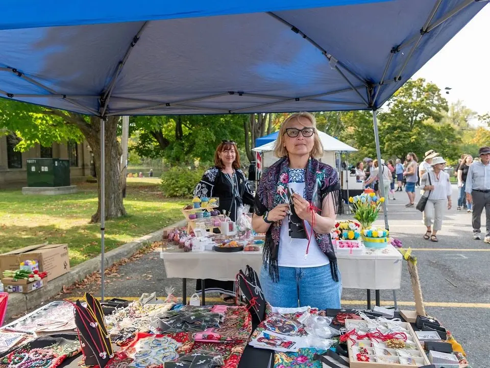 A Ukrainian maker welcoming visitors at a market table filled with jewellery, embroidery and small handmade gifts