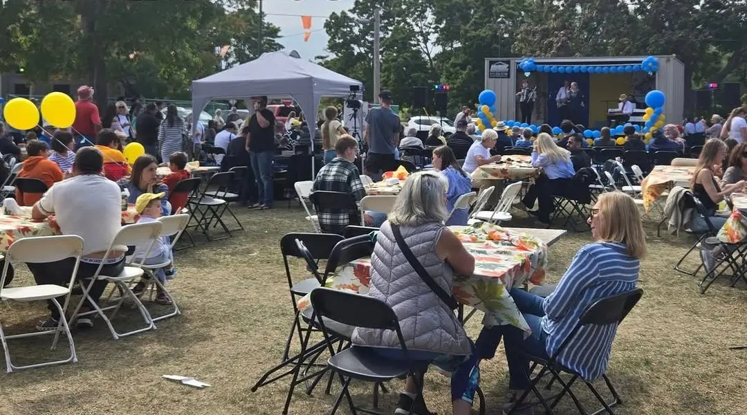 A wide crowd seated at tables with the stage and band in the background, balloon decorations overhead, at UAFest