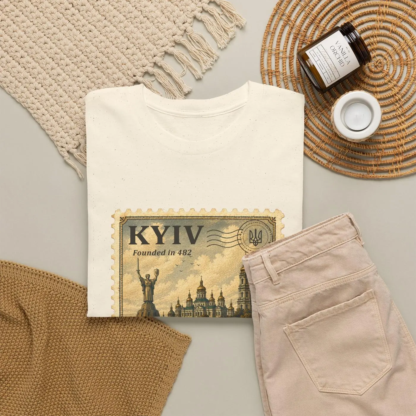 The Kyiv T-shirt folded on a table beside trousers, a woven mat and a small jar