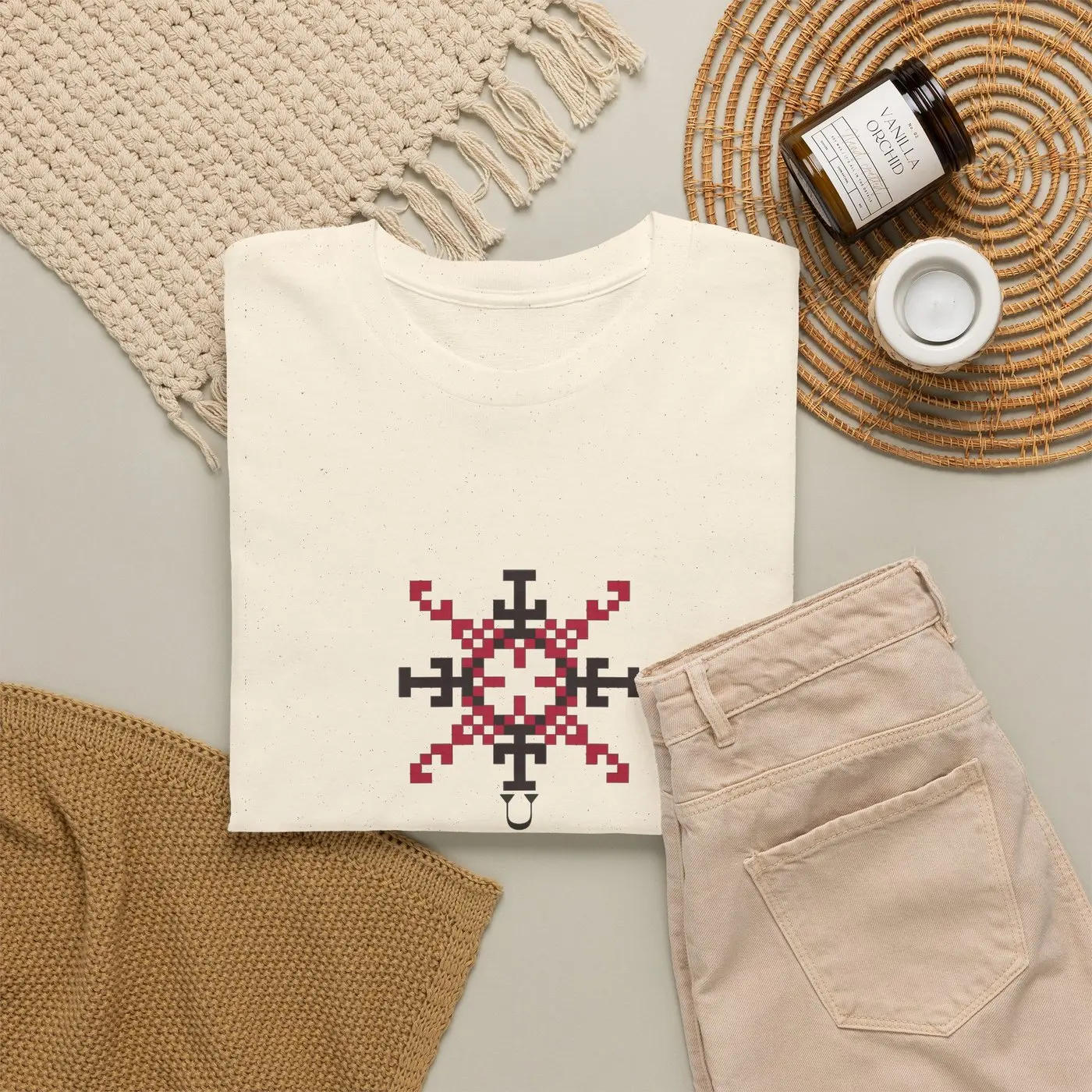 The T-shirt folded on a table beside trousers, a woven mat and a small jar