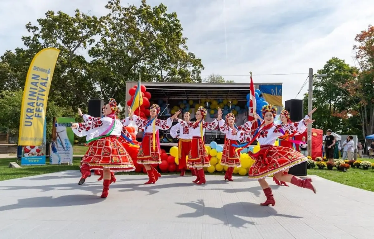 Festivalgoers dancing together on stage, one waving a red and white flag, with a young girl looking on