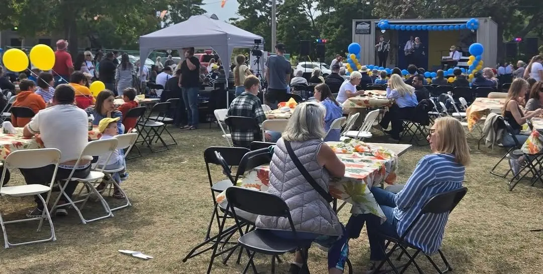 Festivalgoers seated at round tables at UAFest 2024, with a band performing on the balloon-decorated stage behind them