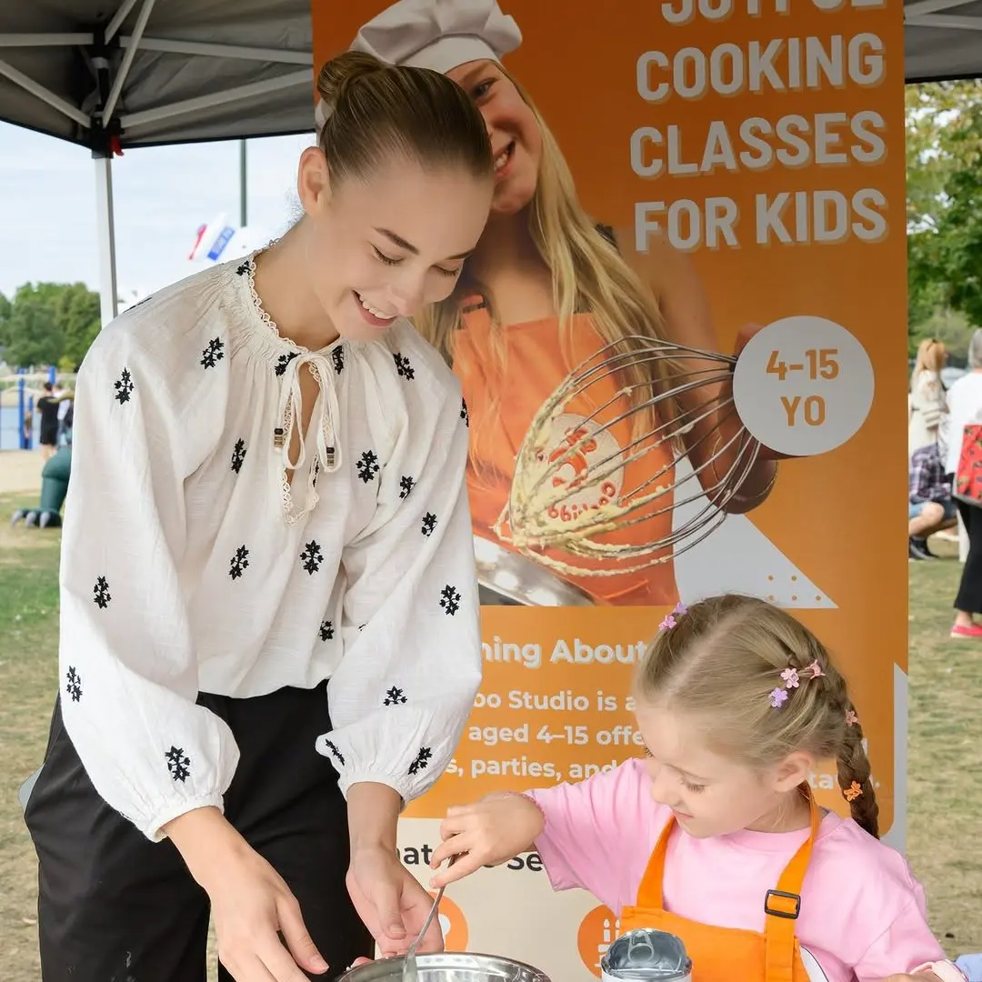 A teen volunteer helping a younger girl whisk batter at the kids' cooking booth run with charity partner Kids of Ukraine