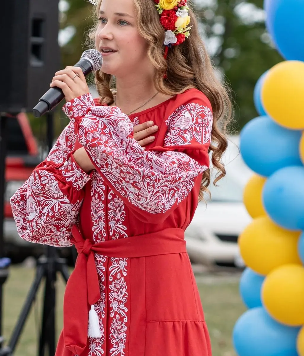 A performer in a red embroidered vyshyvanka dress and floral crown singing on the UAFest stage, framed by blue and yellow balloons