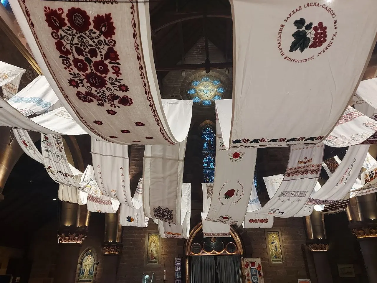 The collective rushnyk hanging across the ceiling of a stone church nave, dozens of embroidered panels visible