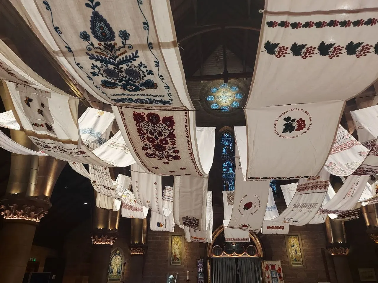 The rushnyk hanging from a church ceiling, stained glass rosette window behind