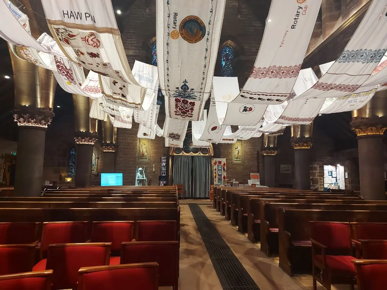 Close-up of embroidered rushnyk panels hanging in a church, including one marked with a Rotary Club emblem