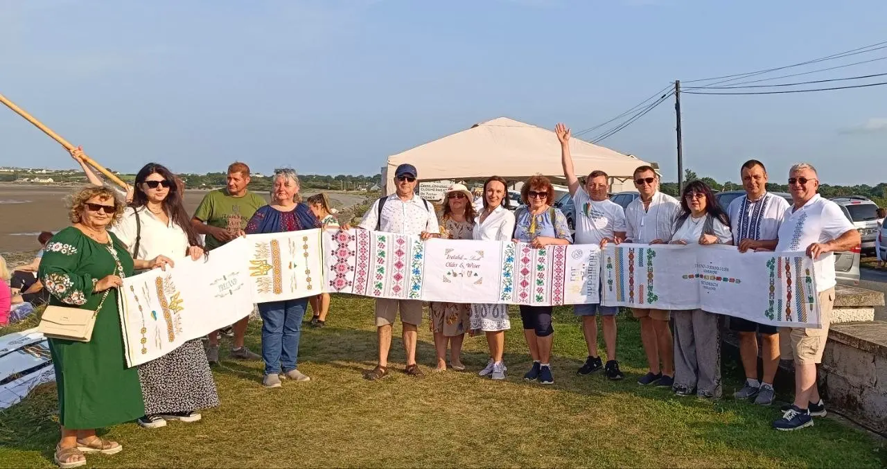 A group of Ukrainian community members in Ireland holding up embroidered sections of the rushnyk outdoors near the sea