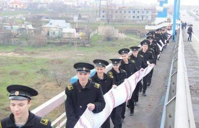 A long line of naval cadets in dress uniform carrying the embroidered rushnyk across a bridge in Kherson, 2014