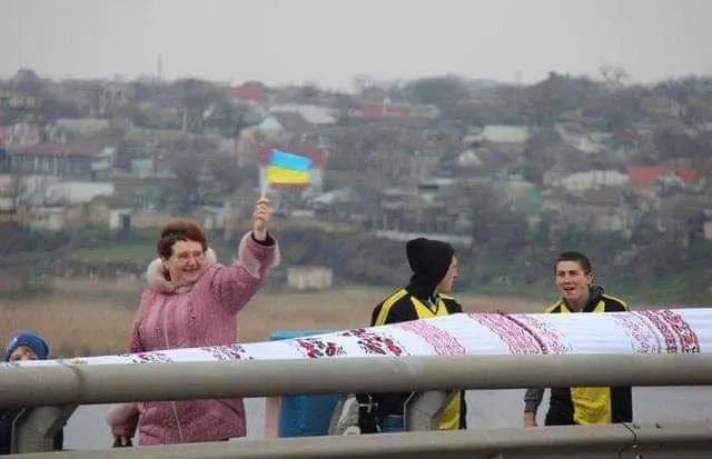 A woman waving a Ukrainian flag over the rushnyk as it stretches across a bridge in Kherson