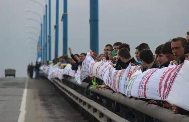 A long line of people stretching the rushnyk along a bridge railing