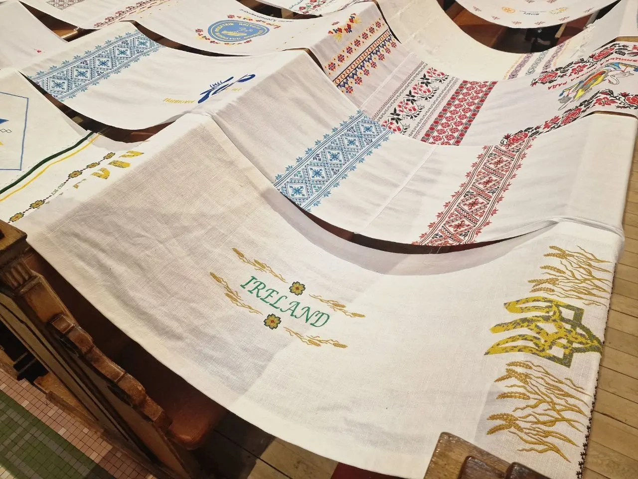 A panel embroidered with the word Ireland in gold wheat ears, laid beside other panels