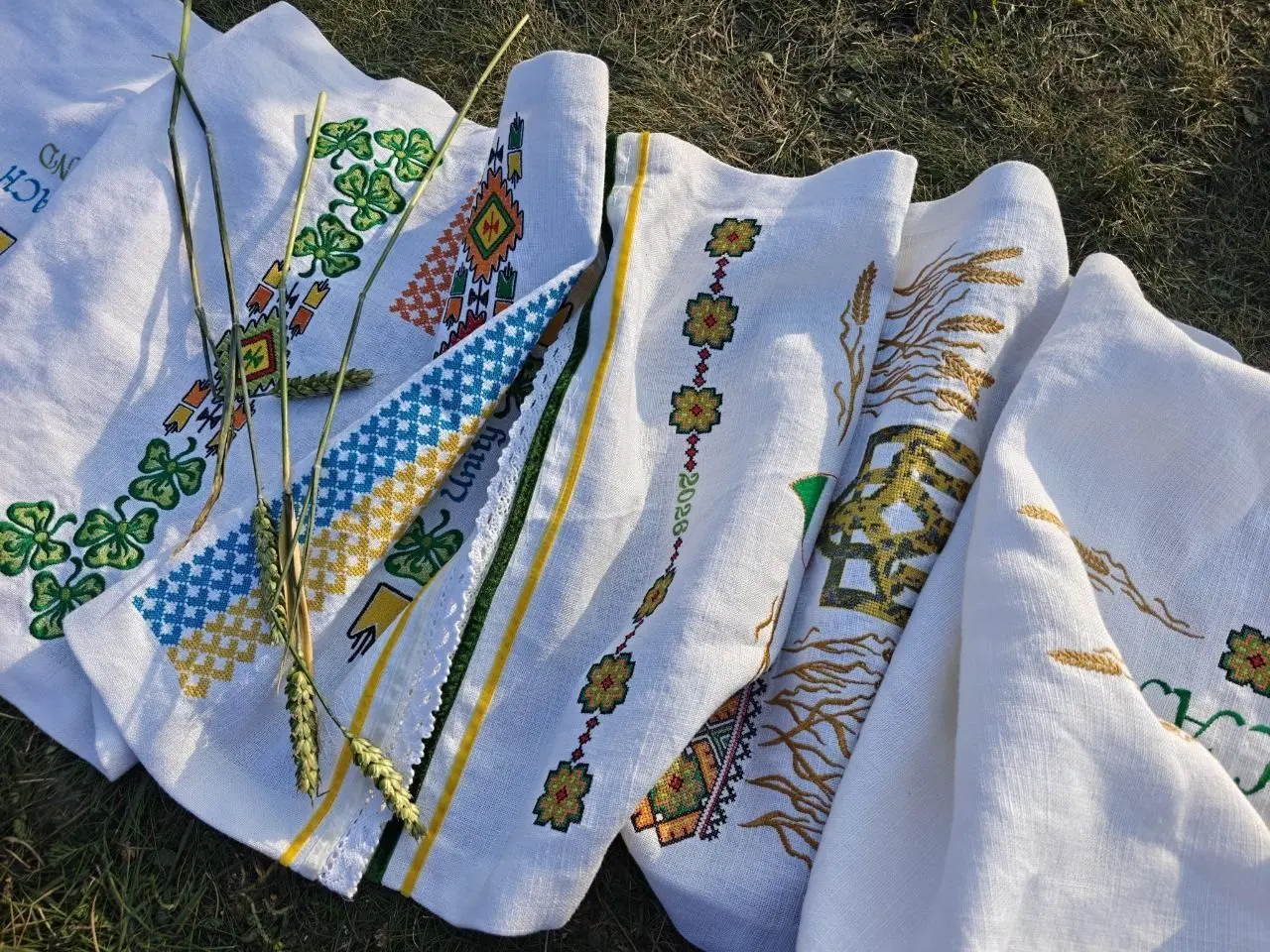 Embroidered panels laid out on grass, blue, yellow and green threads in the light