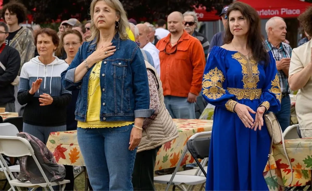Two women embracing at UAFest, one in a denim jacket with a hand on her heart, the other in a blue Ukrainian embroidered dress