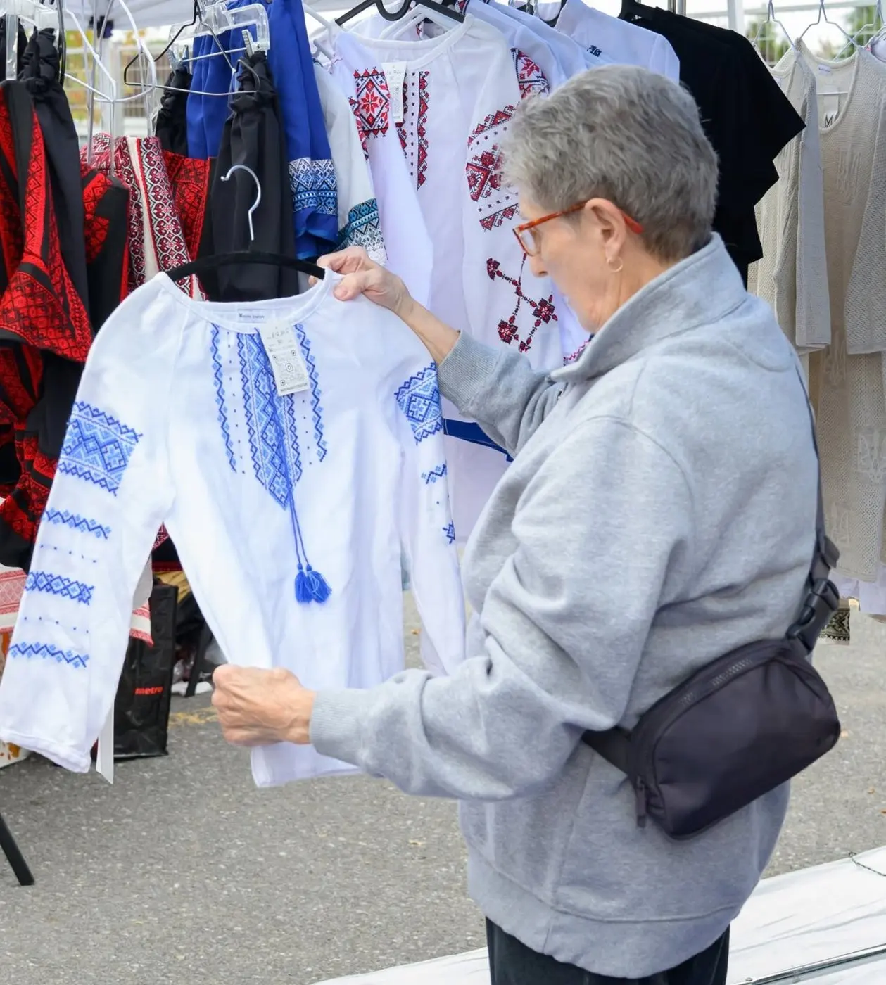 A visitor examining a blue-and-white embroidered shirt at a Ukrainian clothing vendor's market stall
