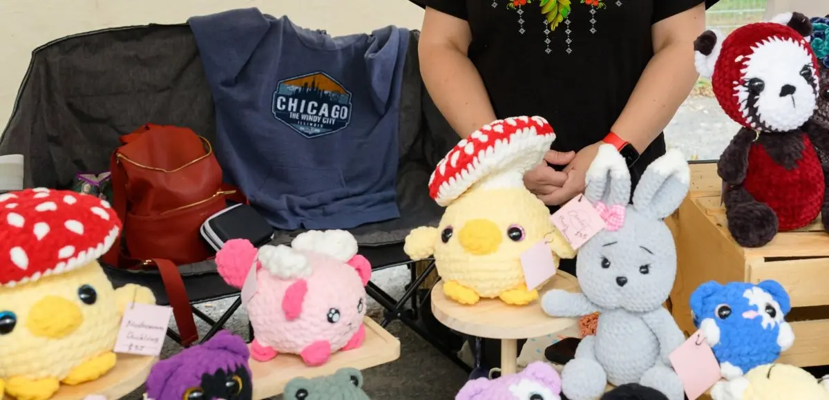 A vendor's tent table set up with handmade crochet toys β mushrooms, chicks, bunnies and a panda β ready for festival visitors