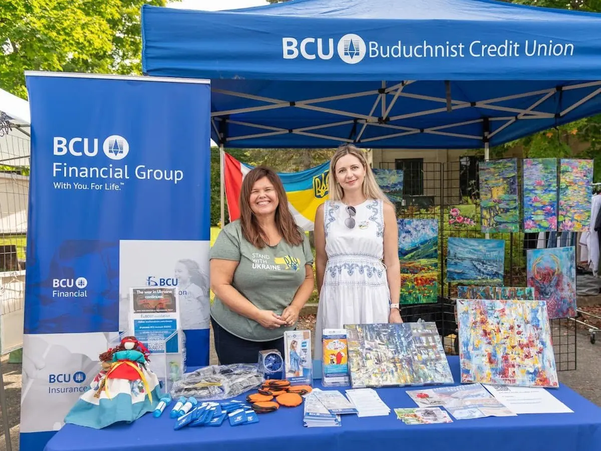 Two representatives welcoming guests at the BCU Financial credit union tent, with artwork and community materials on display