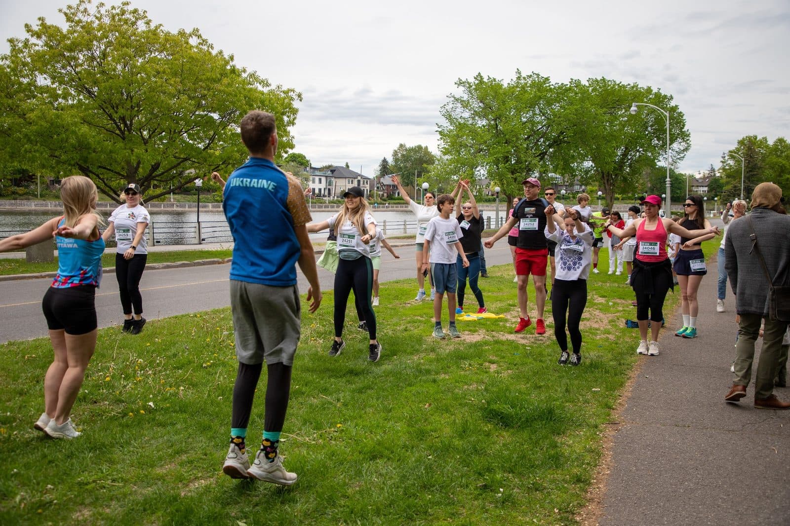Les participants répartis sur la pelouse au bord du canal font un échauffement de groupe avant la course