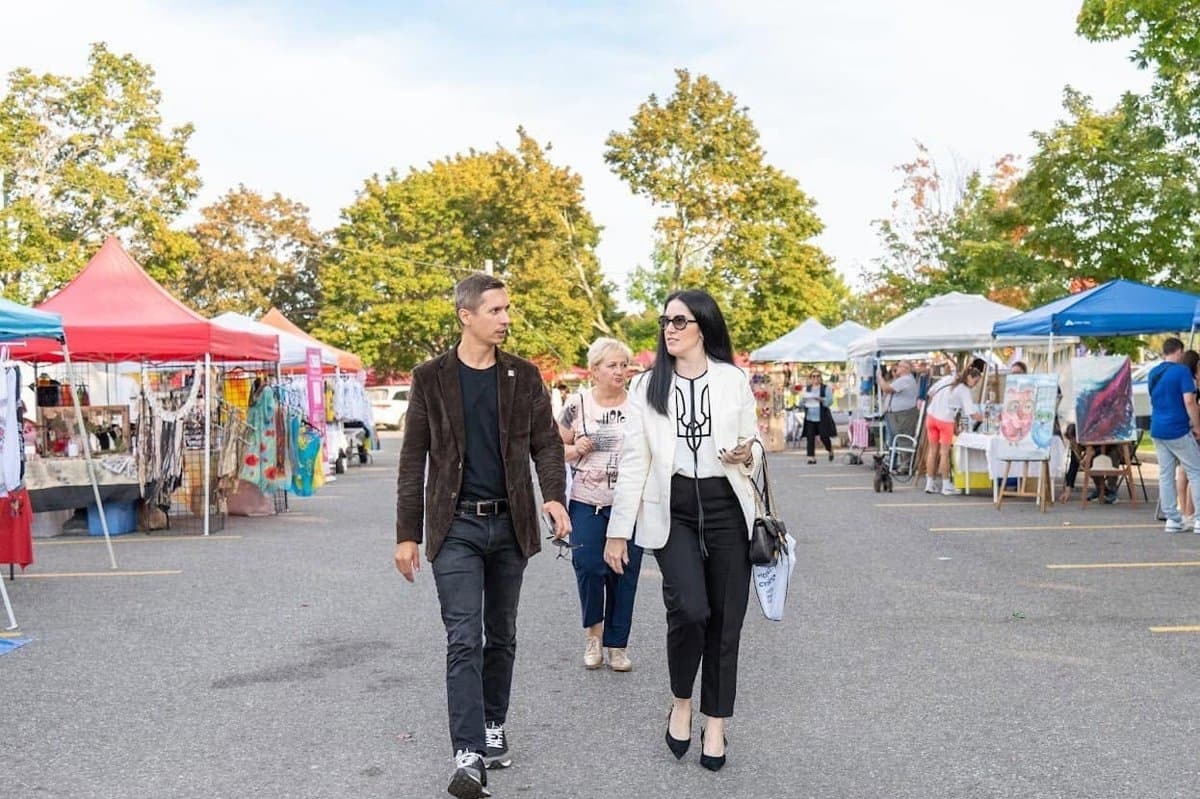 Visitors walking and chatting past the rows of vendor tents at the UAFest festival market