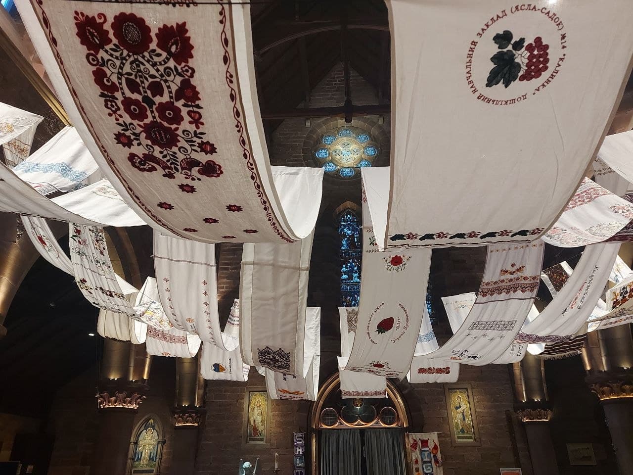 The collective rushnyk hanging across the ceiling of a stone church nave, dozens of embroidered panels visible