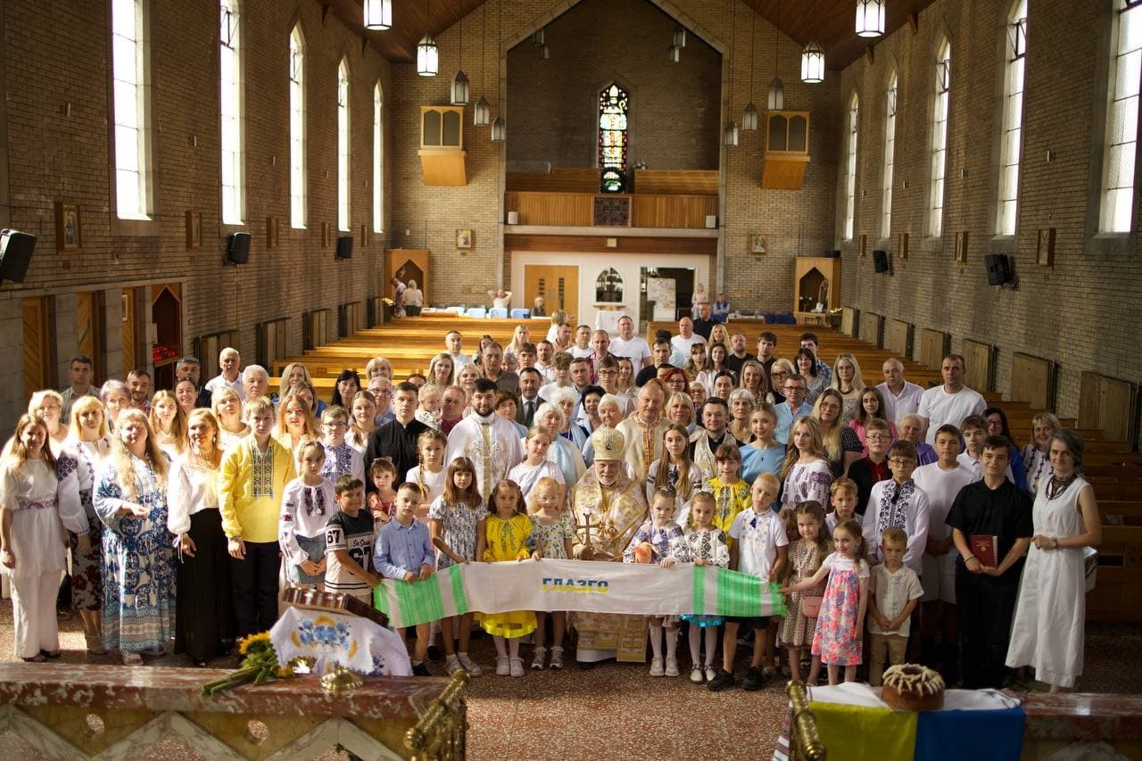 La grande communauté ukrainienne dans l’église, de nombreuses personnes portant des vychyvankas, tenant une longue toile brodée portant l’inscription GLASGOW, au centre — le clergé
