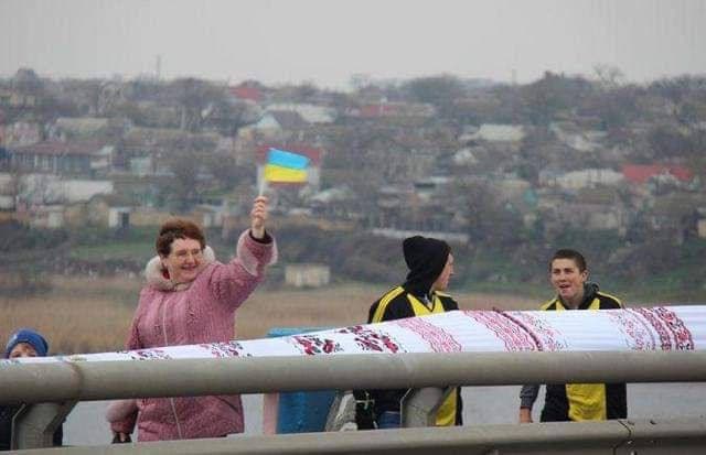 A woman waving a Ukrainian flag over the rushnyk as it stretches across a bridge in Kherson