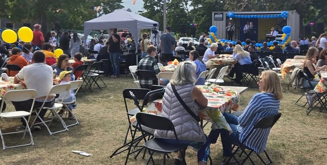 Festivalgoers seated at round tables at UAFest 2024, with a band performing on the balloon-decorated stage behind them