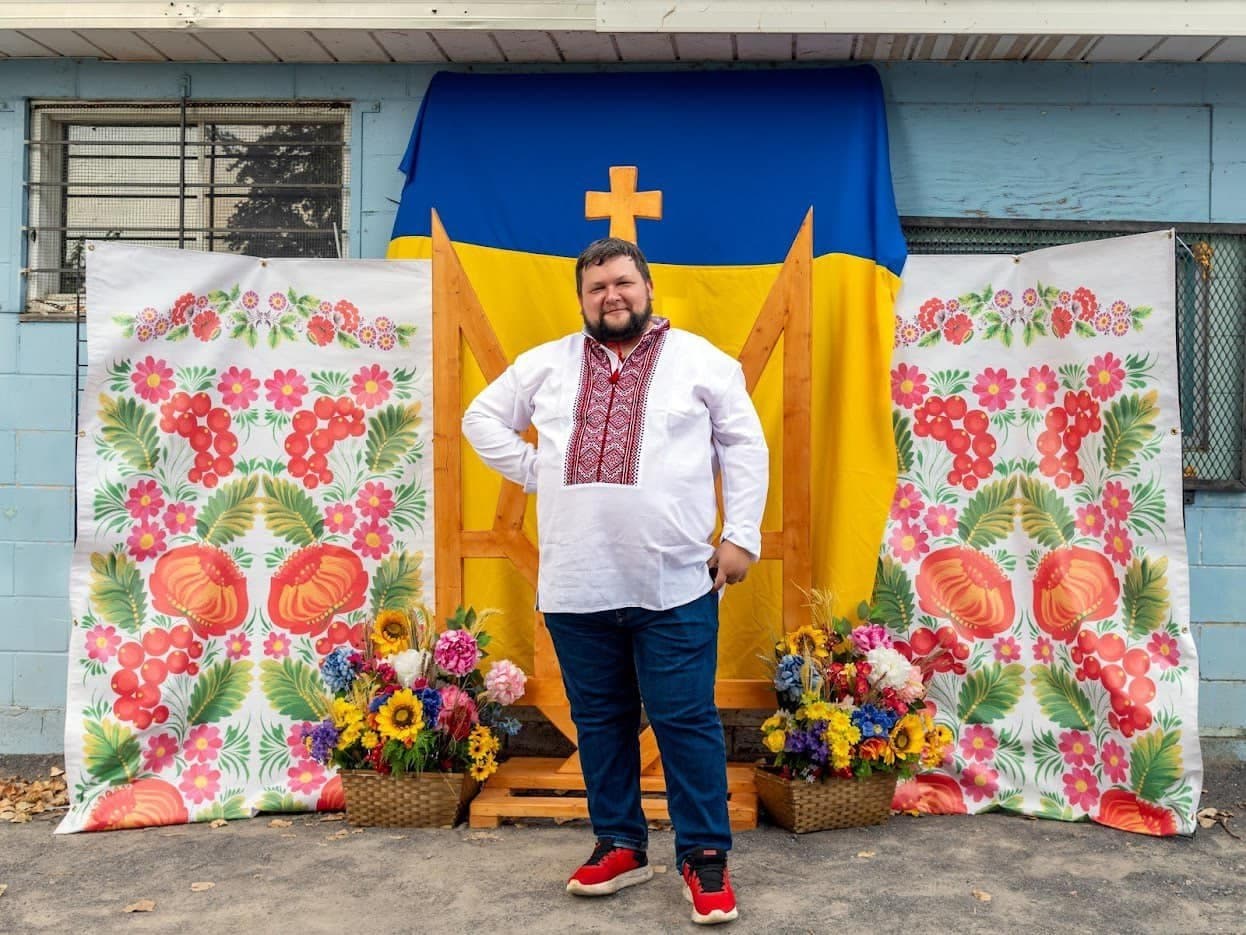 A person in an embroidered Ukrainian vyshyvanka shirt posing in front of a sunflower photo backdrop at a UAFest community event
