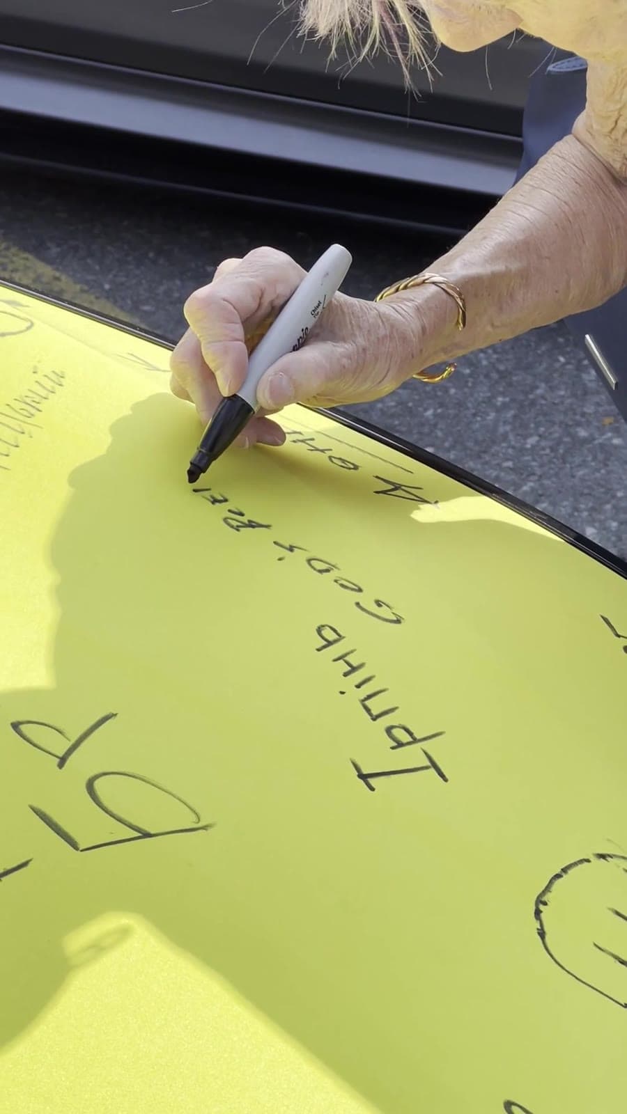 A visitor signing a Ukrainian hometown name on the yellow hood of the flag-painted car at UAFest 2025