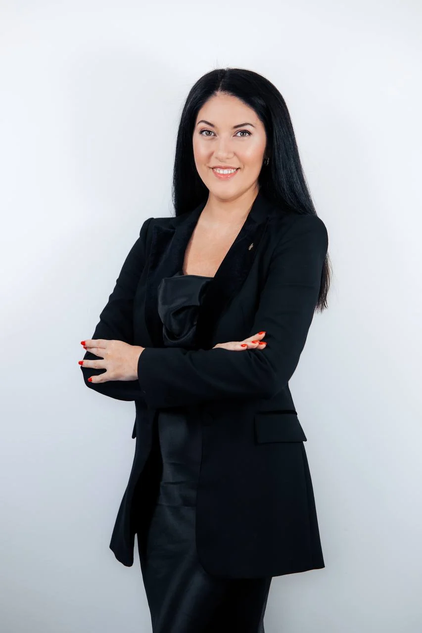Portrait of Anna Kuprieieva in a black suit, arms folded, against a light background