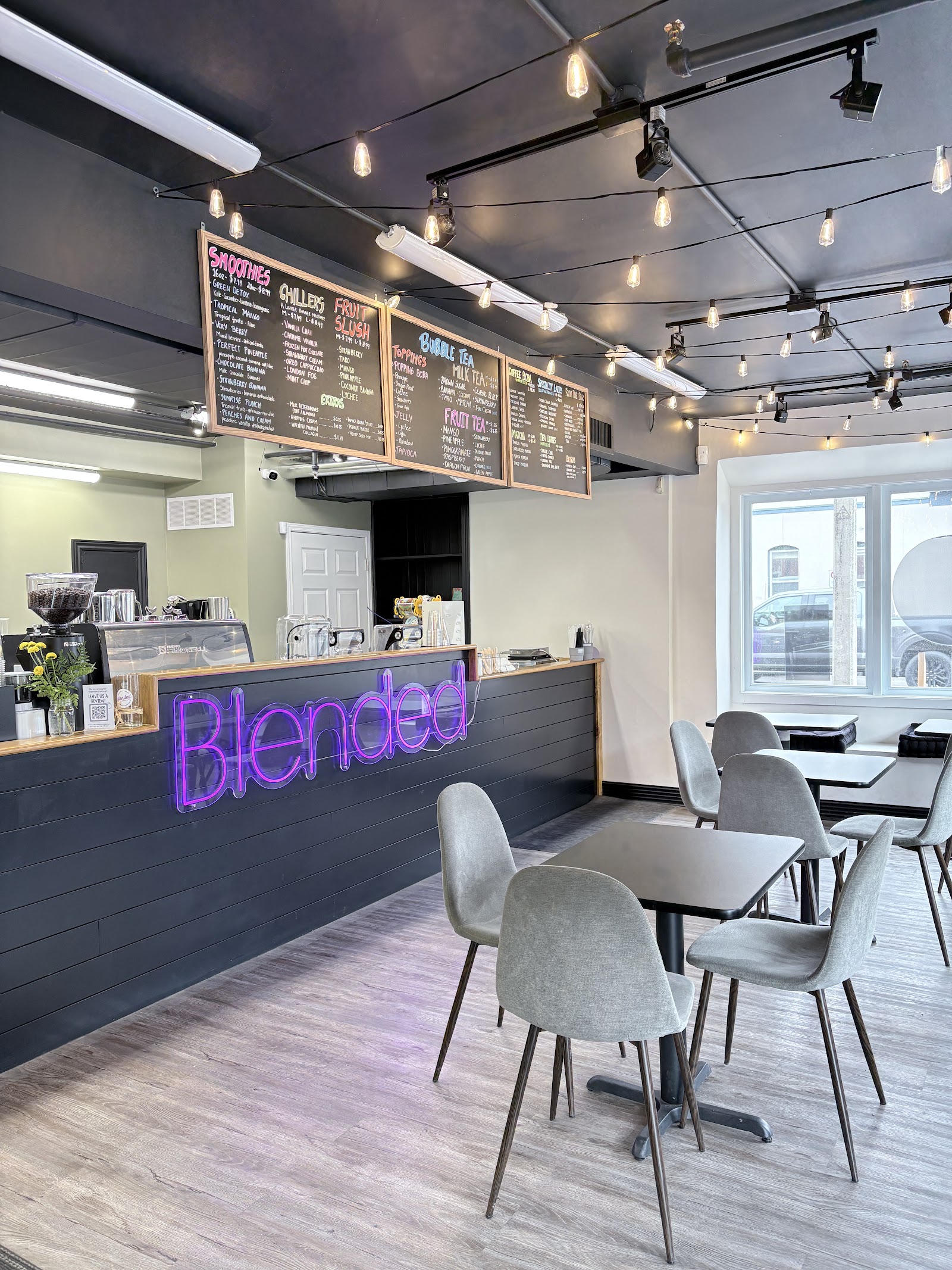 Inside the café: tables and chairs under Edison bulbs, chalkboard menus along the wall, the neon Blended sign on the counter