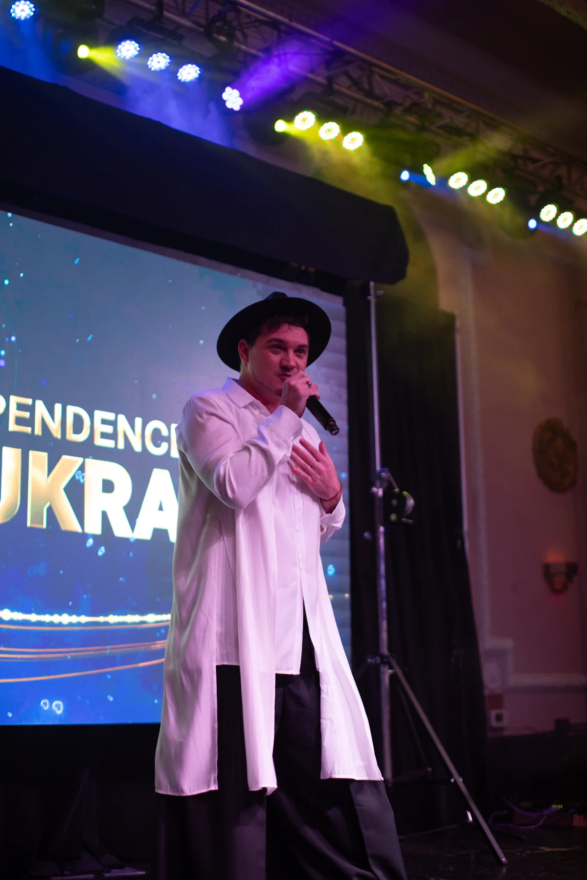 DEN BAURIN singing in a white coat and black hat in front of a screen reading "…PENDENCE" and "UKRA…", from his USA Tour gallery