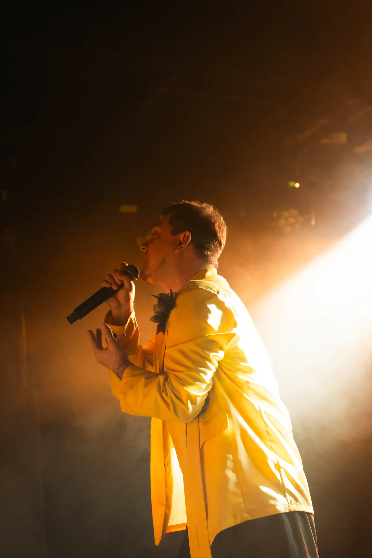 DEN BAURIN in a yellow jacket, lit from behind through stage haze, from his Warsaw concert 2025 gallery