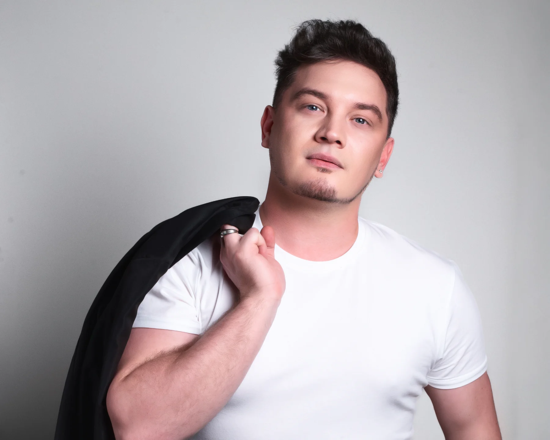 DEN BAURIN in a white t-shirt with a black jacket slung over his shoulder, studio portrait from his "2026" gallery
