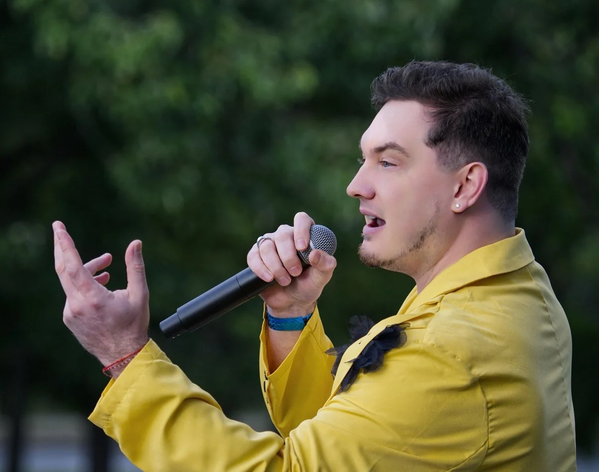 Close-up of DEN BAURIN singing outdoors in a yellow jacket — the cover image of his "Canada Tour 2025" gallery