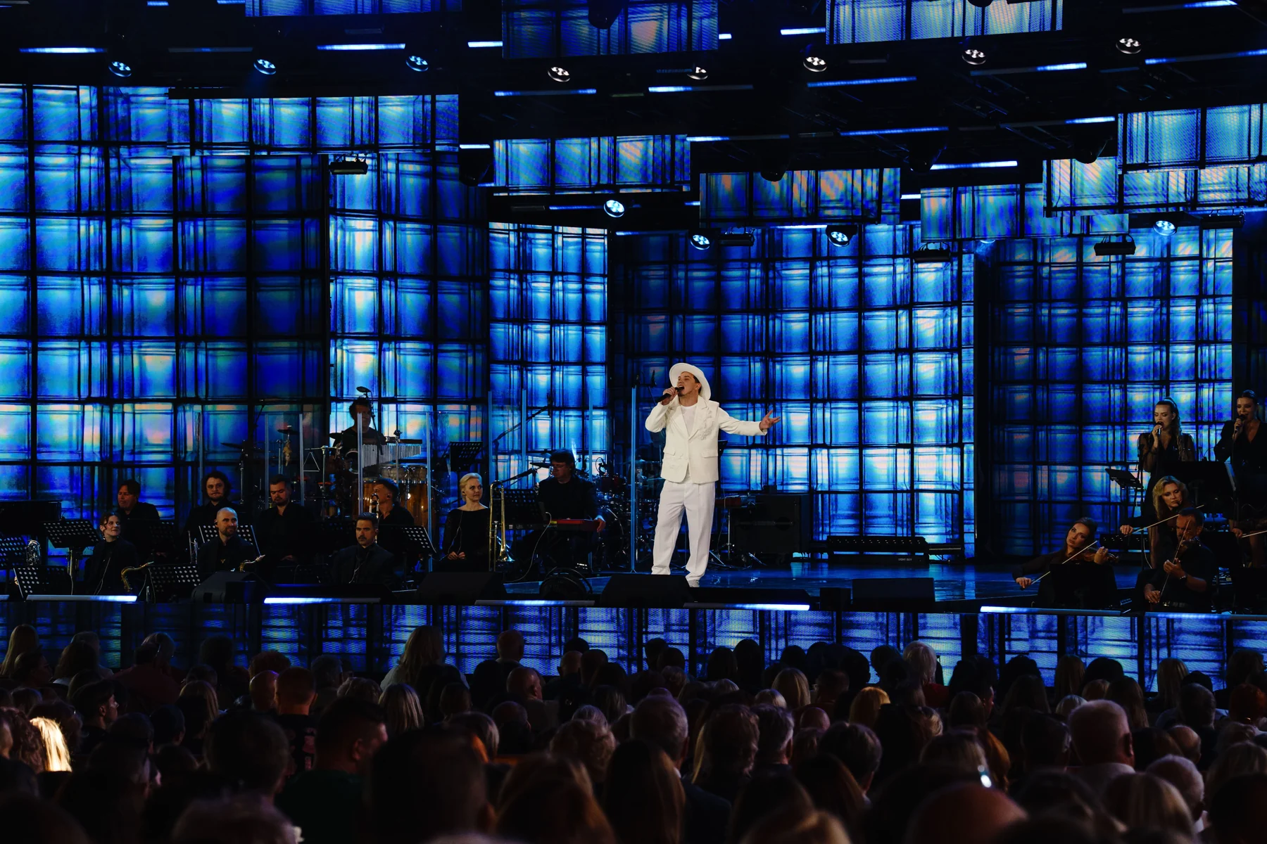 DEN BAURIN alone on a blue-lit stage in front of a seated orchestra and full audience, from his Laima Rendezvous Jurmala 2026 gallery