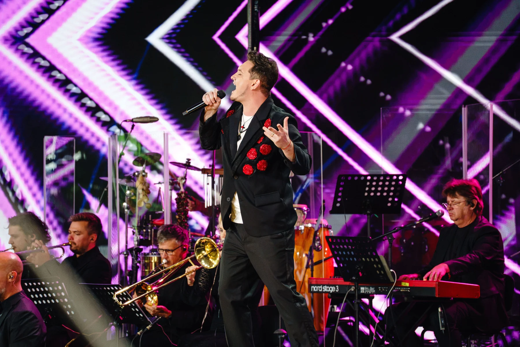 DEN BAURIN performing in a black jacket covered with red roses, backed by a brass section and keyboards, Laima Rendezvous Jurmala 2026