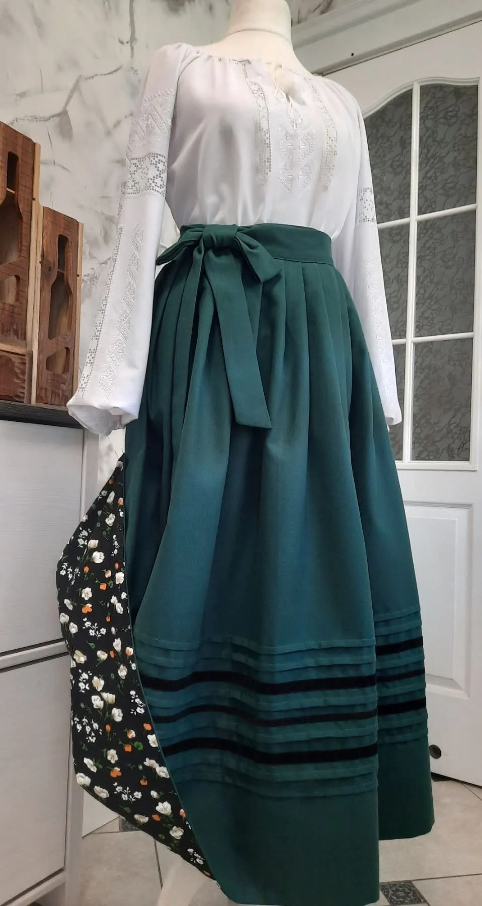 A made-to-order skirt of homespun cloth in deep green, shown on a dress form with an embroidered blouse