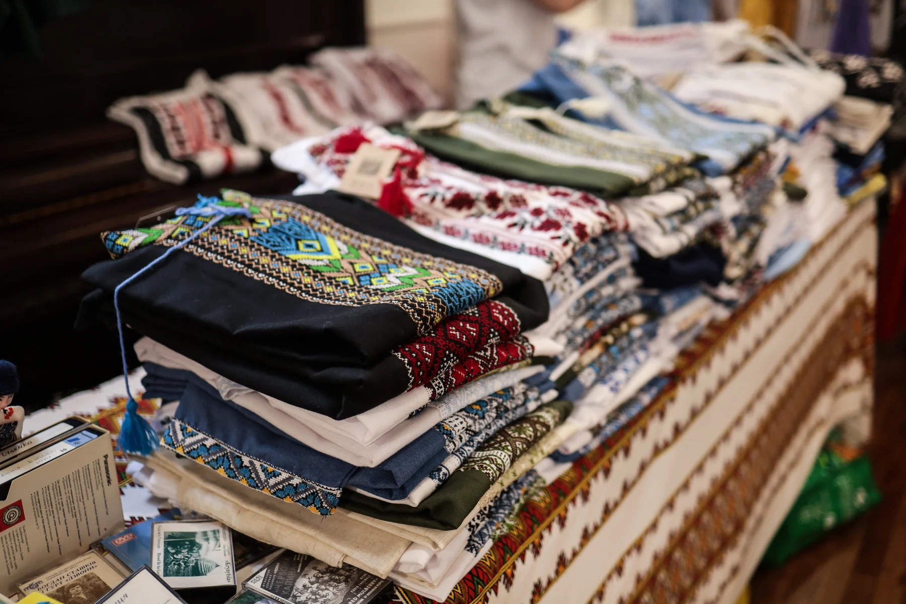 A table stacked with folded vyshyvanky laid out for sale, on an embroidered cloth