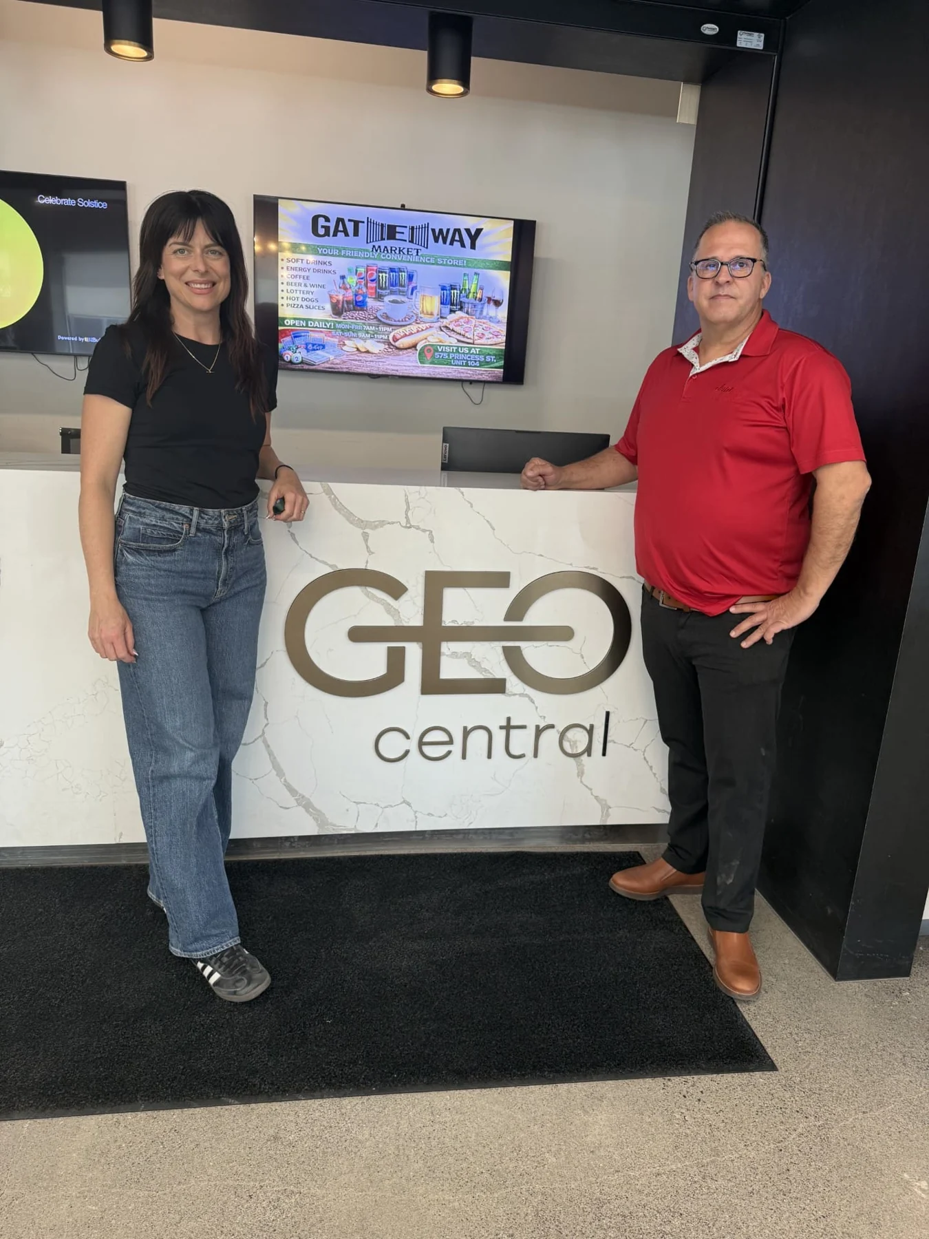 Two people standing on either side of the GEOcentral reception desk in Kingston, beside the brass GEOcentral lettering, at the end of the student turnover cleaning season.