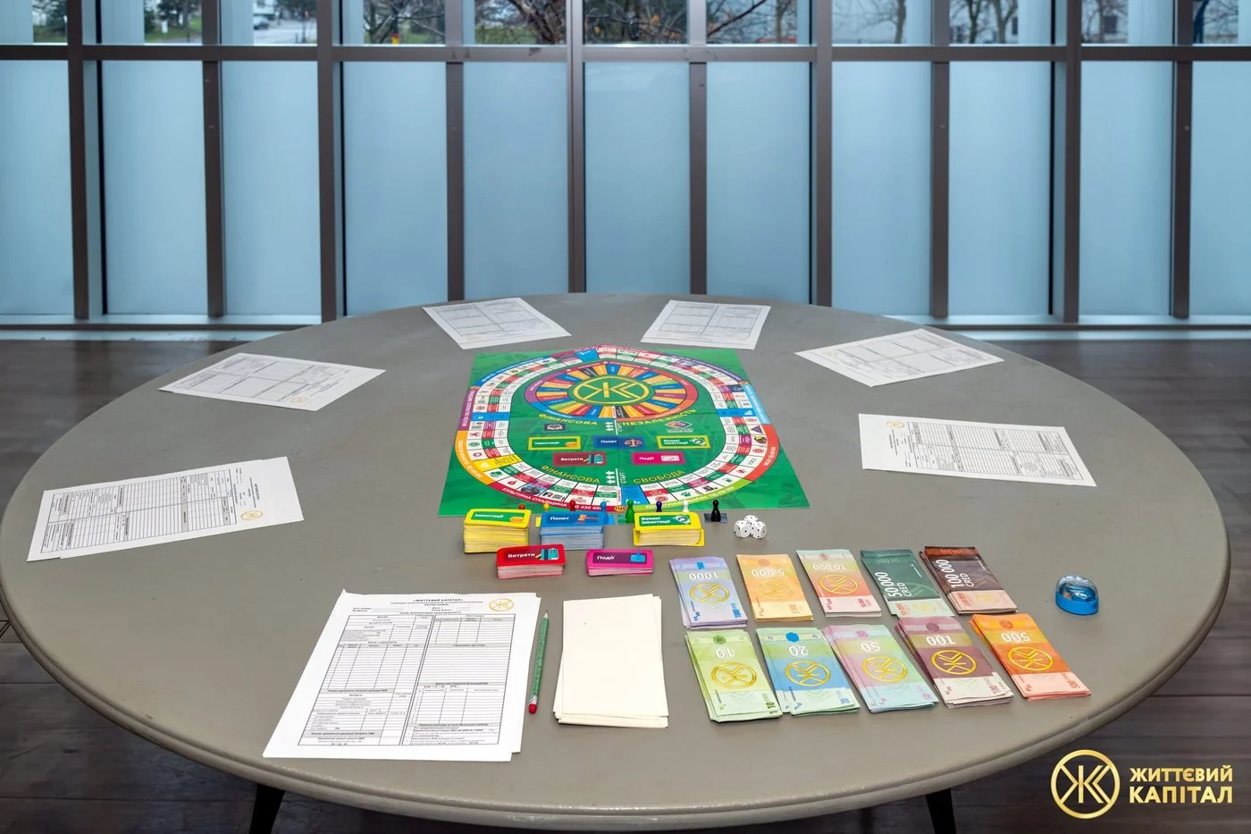 The Life Capital board laid out on a table with player ledger sheets, four card decks and play money around it