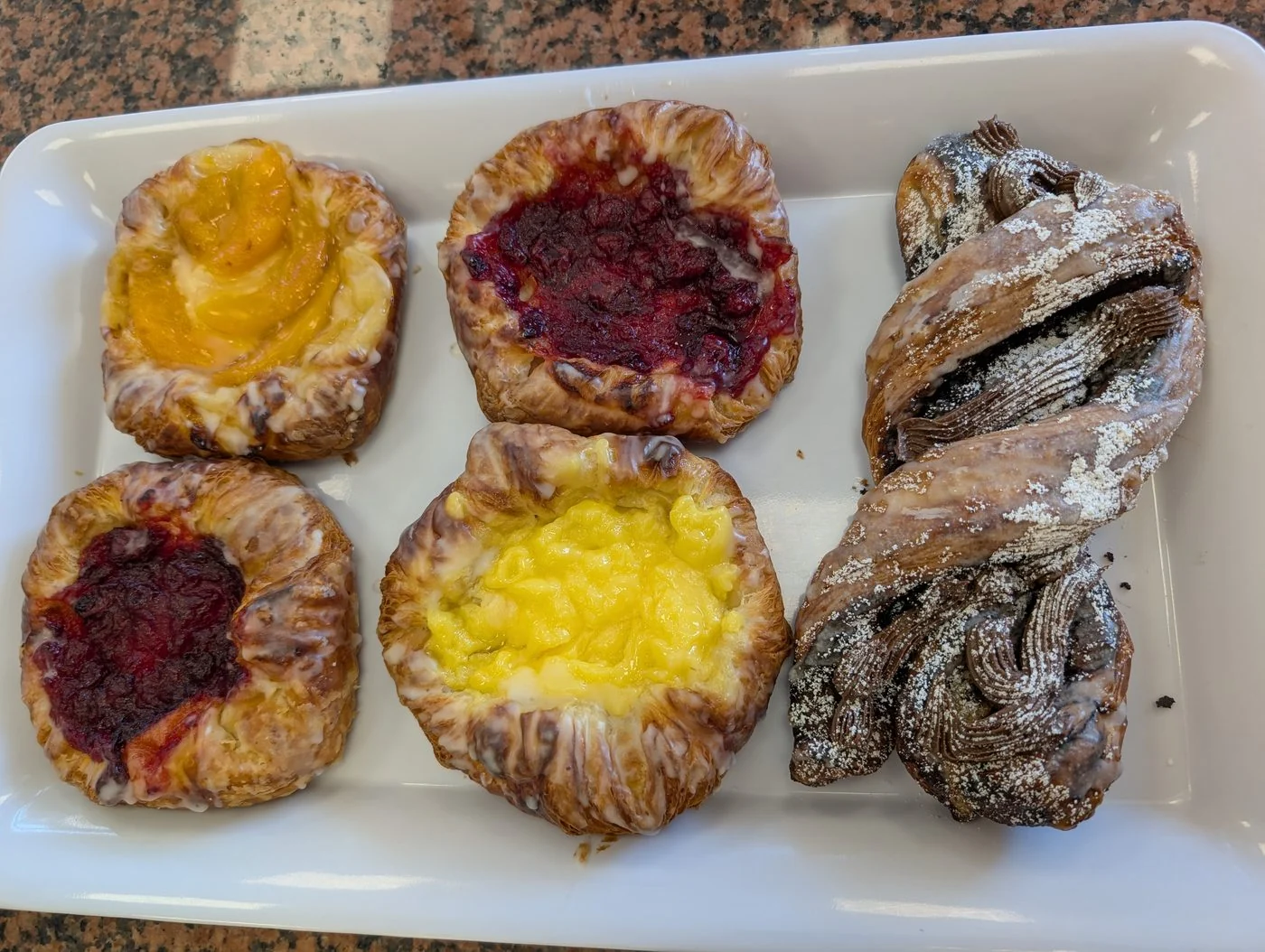 Peach, raspberry and custard danishes on a white tray, with a sugar-dusted chocolate twist.