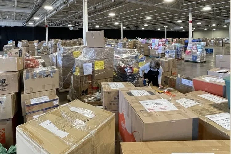 A worker taping up a pallet in a hall filled to the far wall with labelled aid consignments